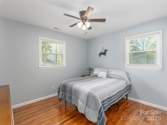 bedroom with baseboards, a ceiling fan, wood finished floors, and visible vents