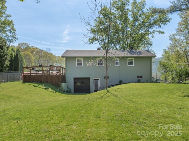 rear view of house with a garage, fence, a wooden deck, and a lawn