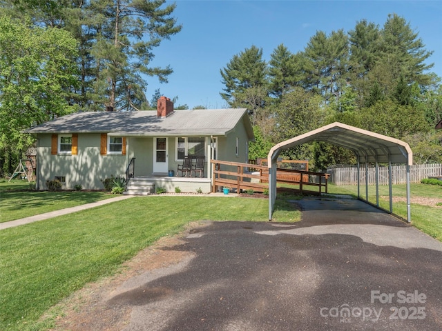 view of front of home with fence, a front lawn, a carport, a chimney, and covered porch