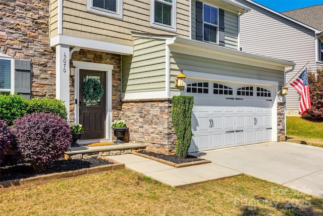 doorway to property featuring concrete driveway, an attached garage, and stone siding