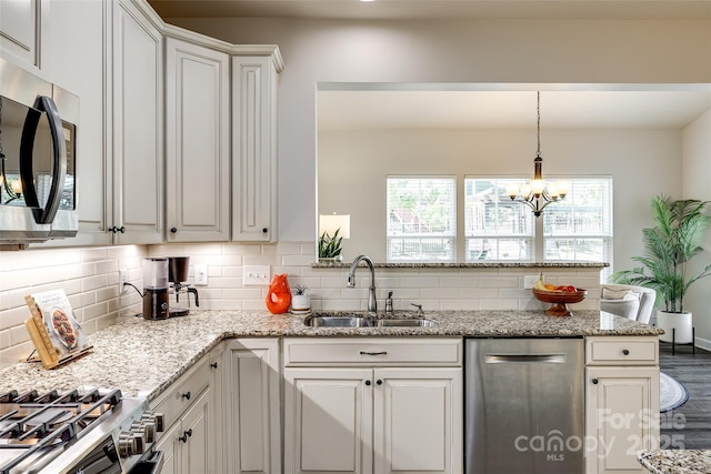 kitchen with decorative backsplash, light stone counters, a sink, appliances with stainless steel finishes, and a notable chandelier