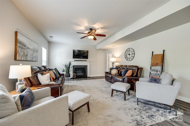 living area featuring baseboards, a fireplace with flush hearth, a ceiling fan, and wood finished floors