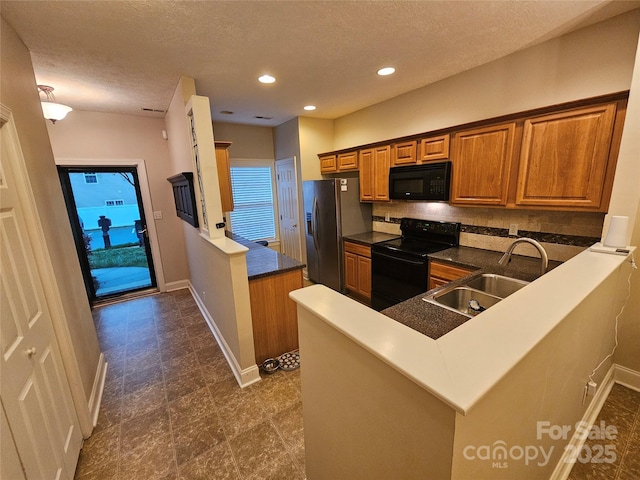 kitchen with a peninsula, brown cabinets, a sink, backsplash, and black appliances