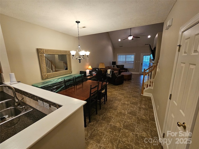 interior space with a textured ceiling, baseboards, lofted ceiling, and ceiling fan with notable chandelier
