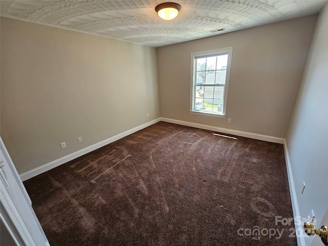 spare room with baseboards, dark carpet, and visible vents