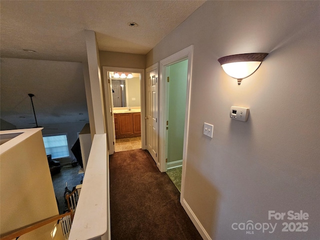 hallway with a textured ceiling, baseboards, and dark carpet