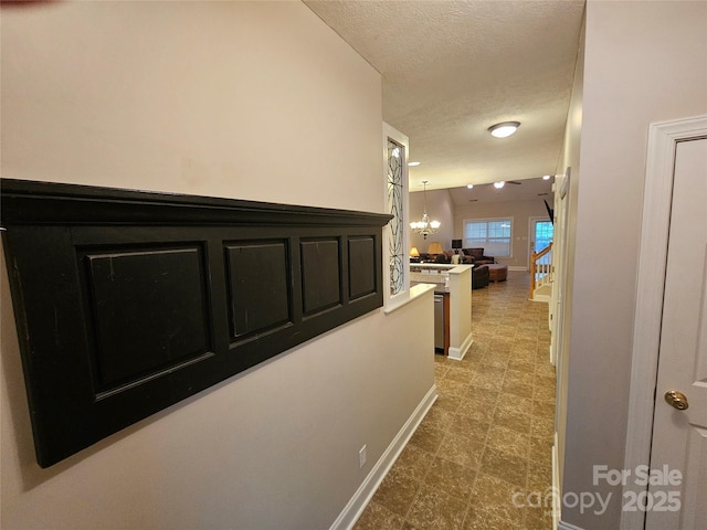 hall with baseboards, a textured ceiling, and an inviting chandelier