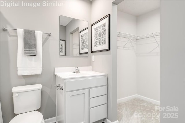 bathroom with vanity, baseboards, toilet, and a walk in closet
