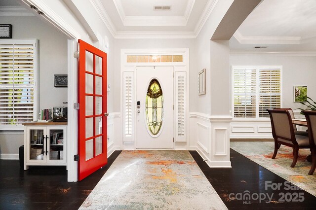 entrance foyer with wood finished floors, visible vents, crown molding, wainscoting, and a raised ceiling