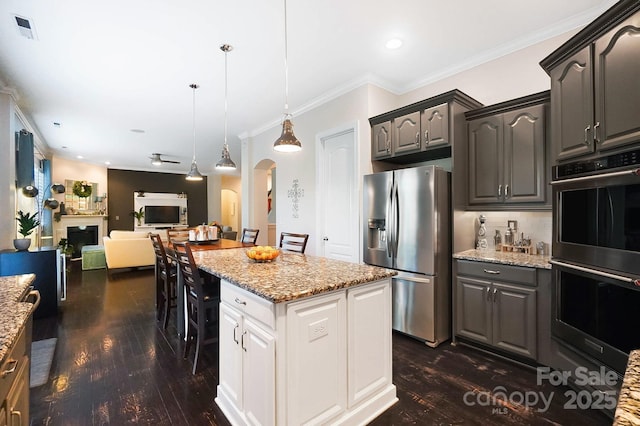 kitchen featuring ornamental molding, appliances with stainless steel finishes, dark wood-type flooring, and arched walkways