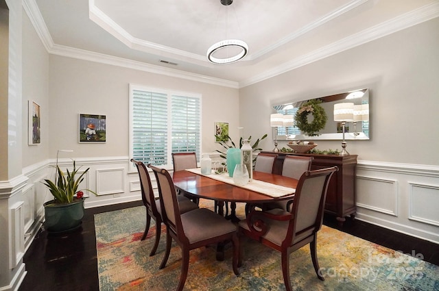 dining room featuring a tray ceiling, ornamental molding, visible vents, a decorative wall, and dark wood-style floors
