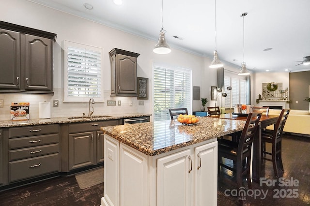 kitchen featuring light stone countertops, dark wood-style flooring, a sink, crown molding, and decorative backsplash