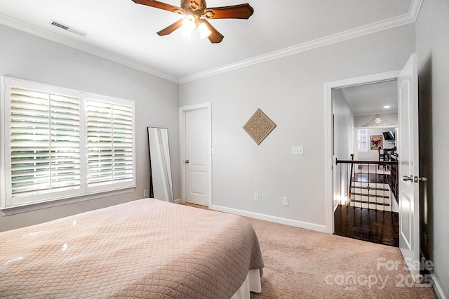 carpeted bedroom with crown molding, visible vents, baseboards, and a ceiling fan