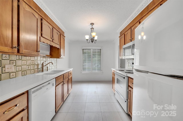 kitchen featuring brown cabinetry, ornamental molding, white appliances, a chandelier, and a sink