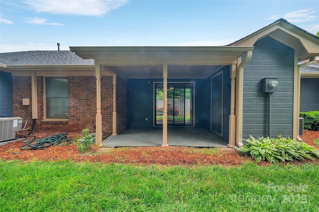 view of exterior entry with a lawn, central AC unit, a patio area, and brick siding