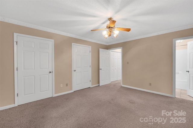 unfurnished bedroom with ornamental molding, baseboards, connected bathroom, a ceiling fan, and carpet