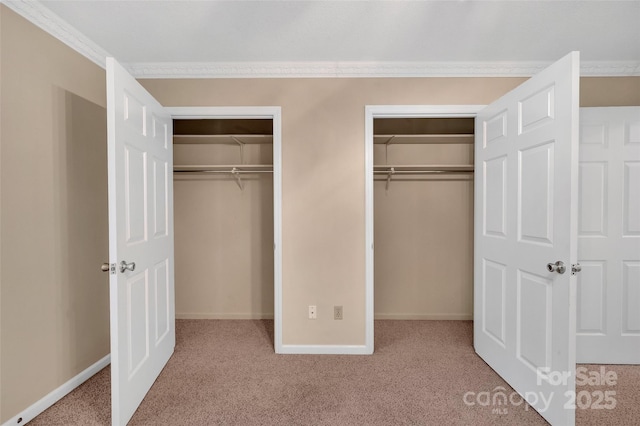 unfurnished bedroom with baseboards, ornamental molding, carpet, and two closets