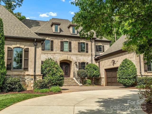 french provincial home featuring driveway, roof with shingles, a garage, stone siding, and stucco siding