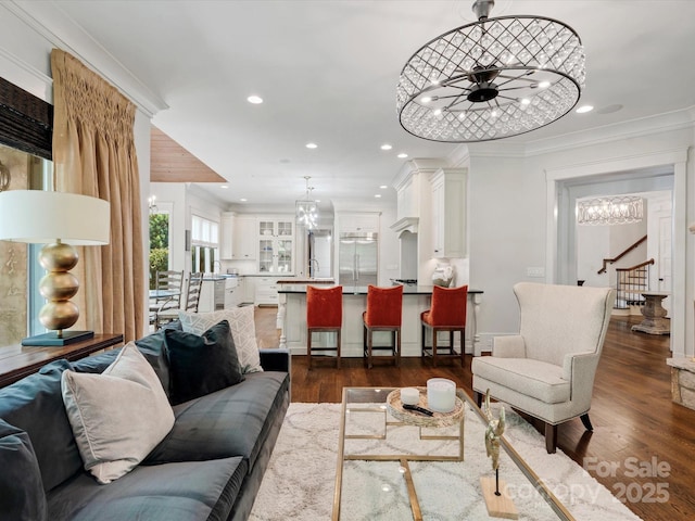 living room featuring ornamental molding, stairs, recessed lighting, dark wood finished floors, and ceiling fan with notable chandelier
