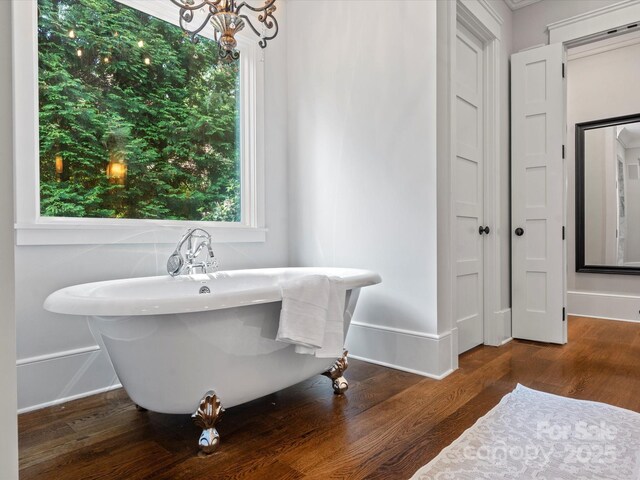 bathroom with a freestanding tub, baseboards, wood finished floors, and a notable chandelier