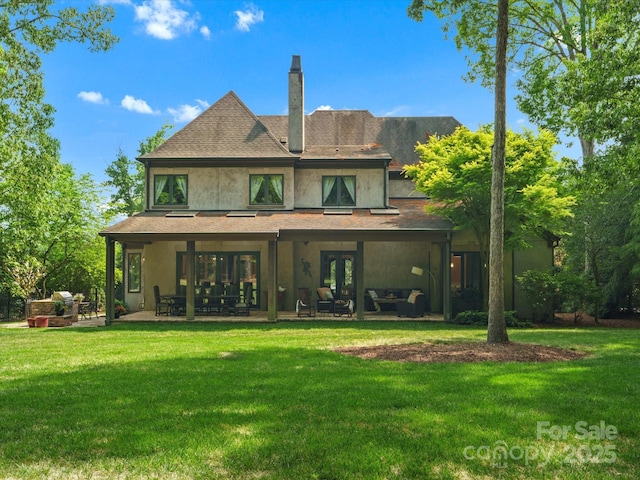 back of property featuring a lawn, stucco siding, a chimney, and a patio