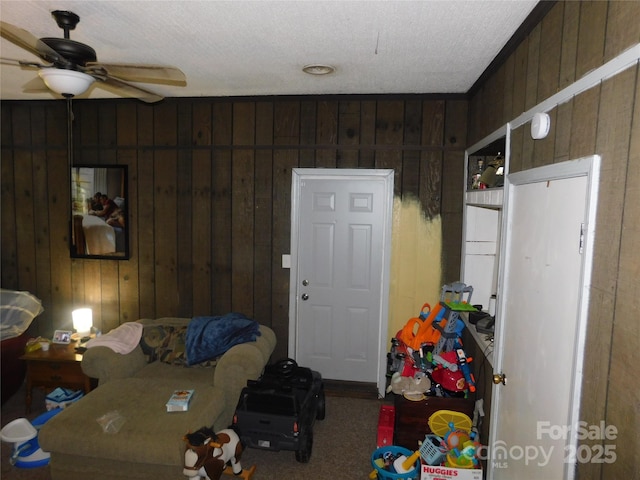 carpeted living area featuring a textured ceiling, wood walls, and a ceiling fan