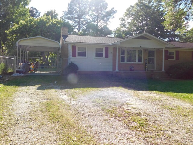 ranch-style house with a chimney, dirt driveway, fence, and a carport
