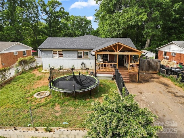back of house with a lawn, fence, a trampoline, and brick siding