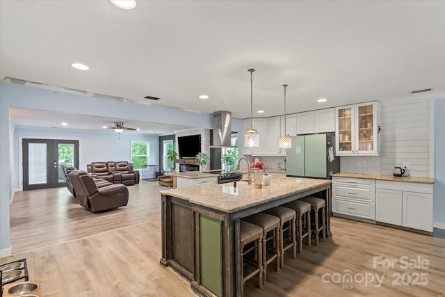 kitchen featuring light wood-style floors, white cabinets, freestanding refrigerator, and an island with sink
