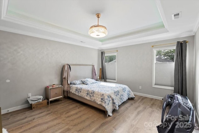 bedroom featuring visible vents, ornamental molding, light wood-style floors, baseboards, and a tray ceiling