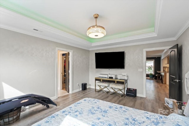 bedroom featuring visible vents, ornamental molding, wood finished floors, and a tray ceiling