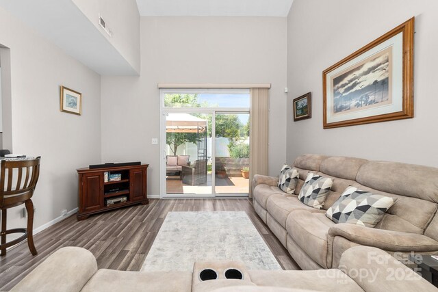 living area with baseboards, visible vents, wood finished floors, and a high ceiling