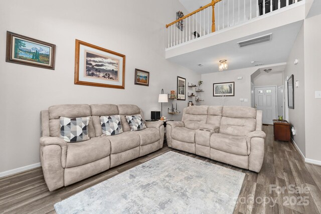 living room featuring baseboards, visible vents, wood finished floors, and a towering ceiling