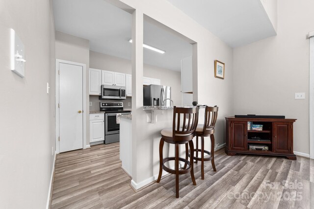 kitchen featuring a breakfast bar, baseboards, white cabinets, light wood-style flooring, and appliances with stainless steel finishes