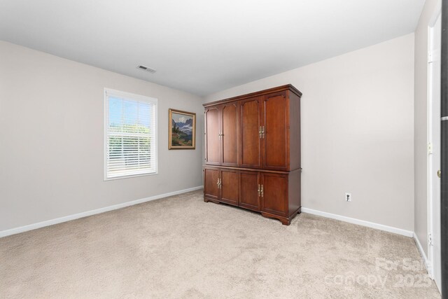 unfurnished bedroom featuring baseboards, light colored carpet, and visible vents