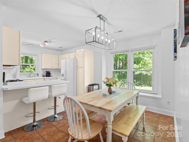 dining area with an inviting chandelier, a textured ceiling, baseboards, light tile patterned floors, and visible vents