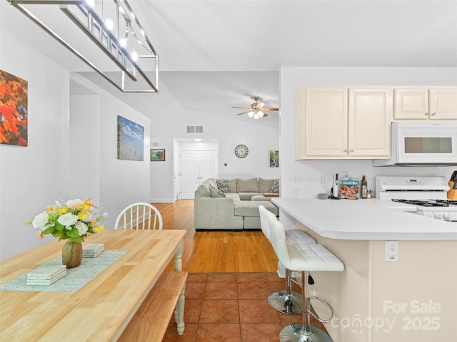 kitchen featuring visible vents, lofted ceiling, white appliances, light countertops, and a ceiling fan