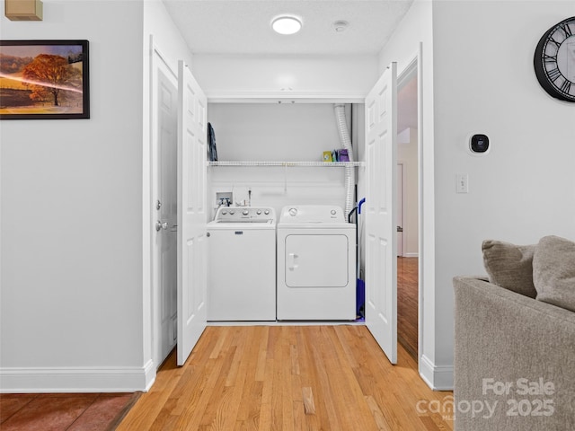 clothes washing area featuring baseboards, laundry area, light wood finished floors, and washing machine and clothes dryer