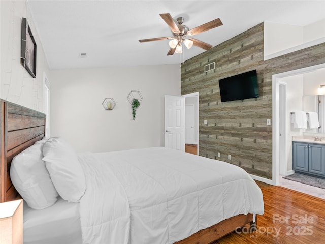 bedroom featuring visible vents, vaulted ceiling, wood walls, wood finished floors, and an accent wall