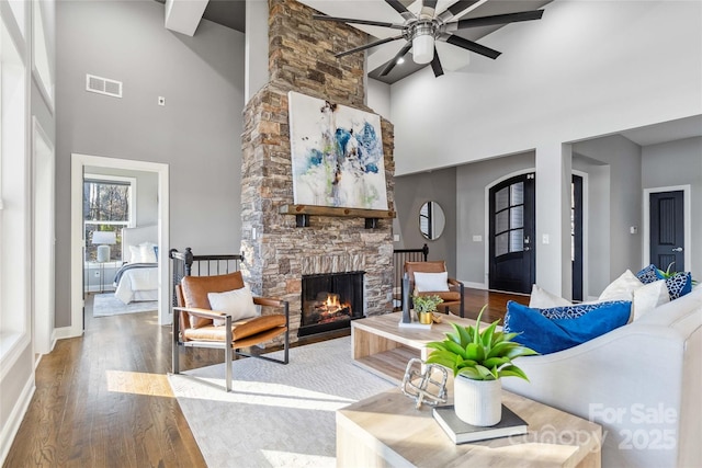 living area featuring visible vents, wood finished floors, a fireplace, high vaulted ceiling, and a ceiling fan