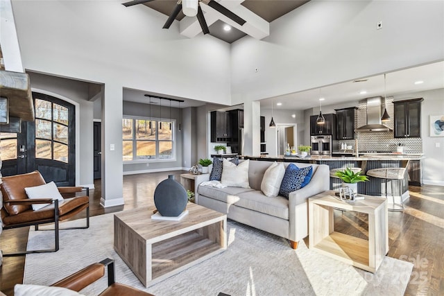 living room with a towering ceiling, beamed ceiling, baseboards, ceiling fan, and light wood-style flooring