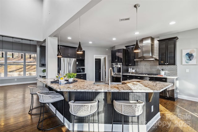 kitchen featuring baseboards, dark wood-style floors, wall chimney exhaust hood, backsplash, and stainless steel appliances
