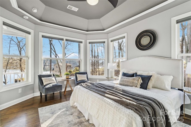 bedroom with visible vents, a raised ceiling, baseboards, and wood finished floors