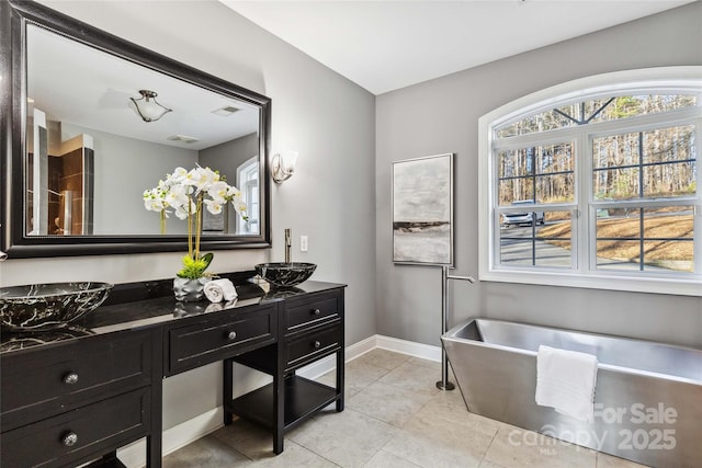 bathroom featuring double vanity, a freestanding bath, tile patterned flooring, a sink, and baseboards