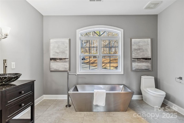 bathroom featuring visible vents, baseboards, vanity, toilet, and a soaking tub