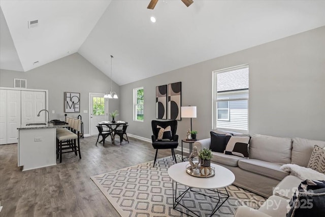 living room with visible vents, wood finished floors, baseboards, high vaulted ceiling, and ceiling fan with notable chandelier