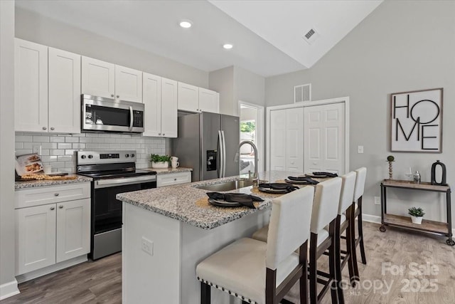 kitchen with visible vents, appliances with stainless steel finishes, light wood-type flooring, a sink, and an island with sink