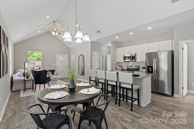 dining area featuring baseboards, light wood-style flooring, ceiling fan with notable chandelier, and high vaulted ceiling