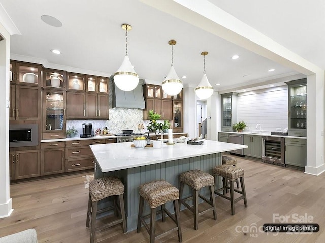 kitchen featuring appliances with stainless steel finishes, a breakfast bar, light countertops, premium range hood, and wine cooler