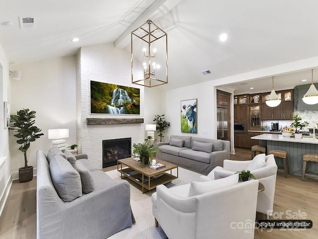 living room featuring visible vents, beamed ceiling, a fireplace, and light wood-type flooring